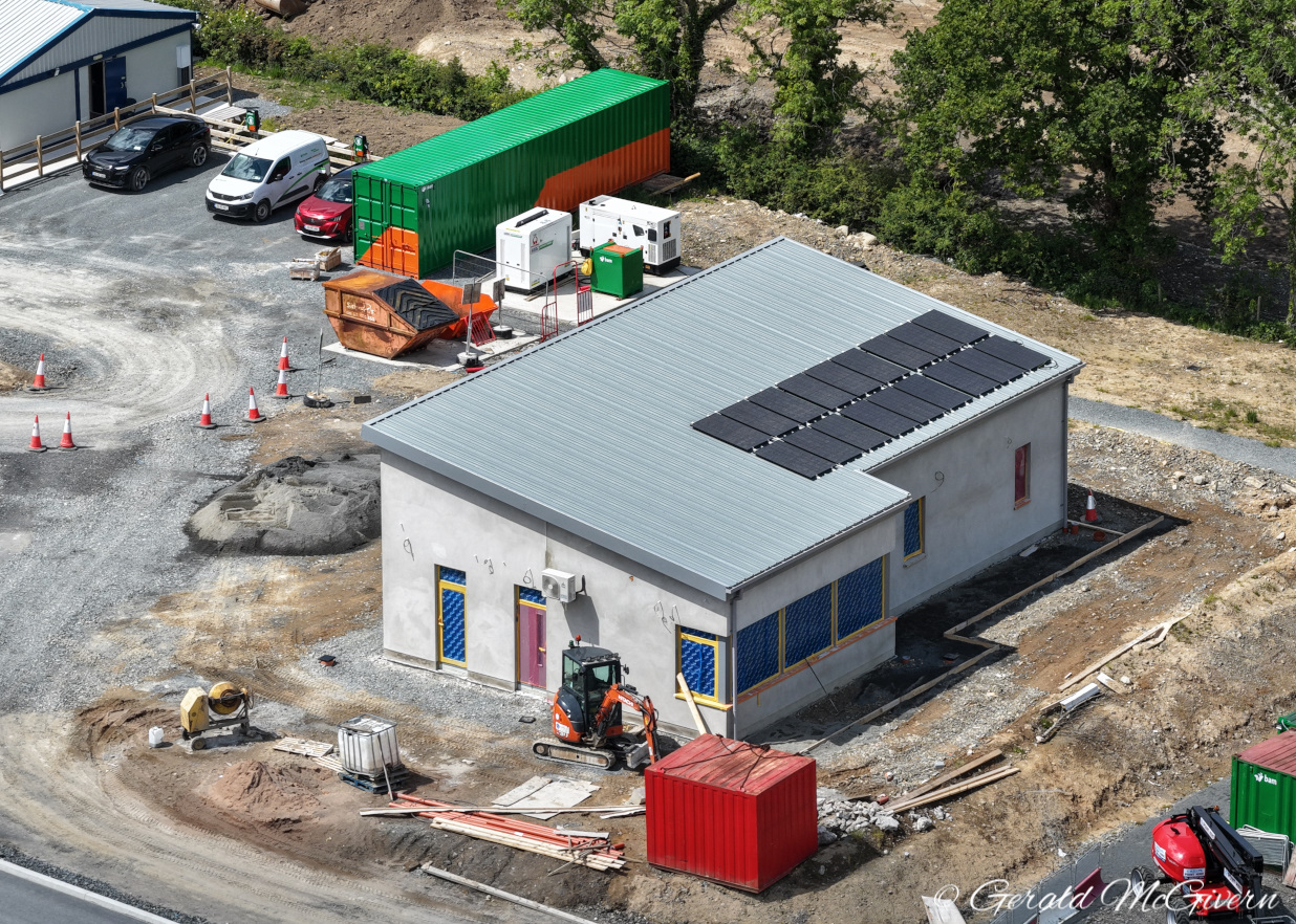 Aerial view of a white concrete building
                          with a grey metal roof with solar panels, and
                          construction machinery around it. The windows
                          are blocked up.