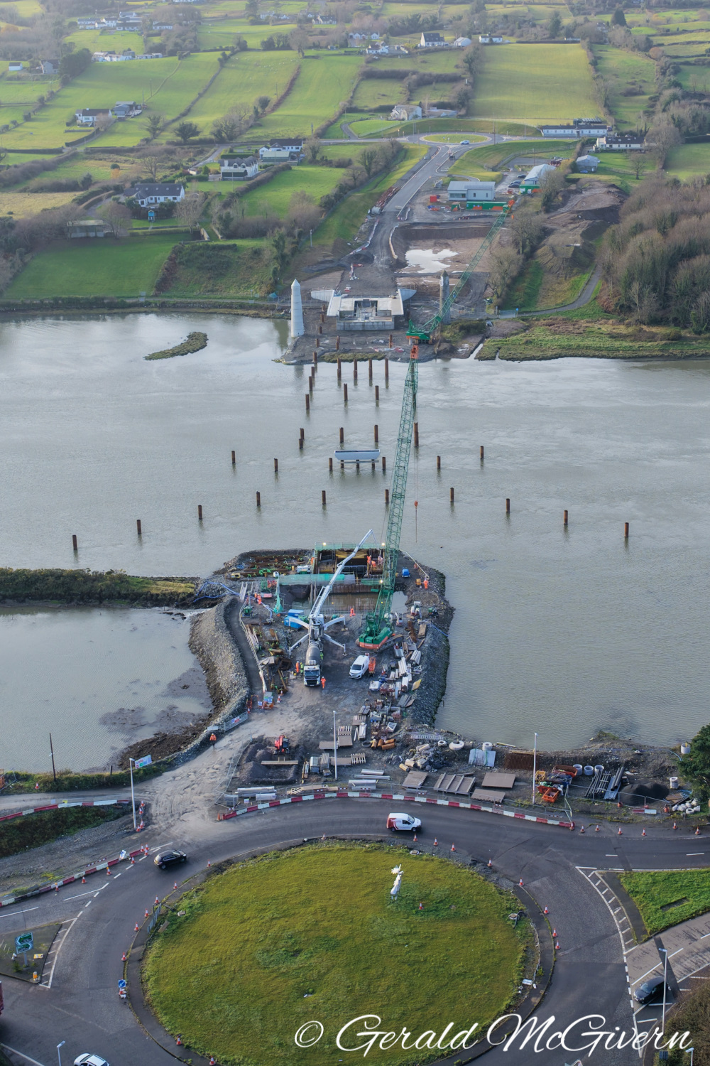 River crosses image left-right. In
                          foreground is a bridge abutment being built
                          with two cranes. Beyond the river is a second
                          abutment. The river has about 20 steel piles
                          in it.