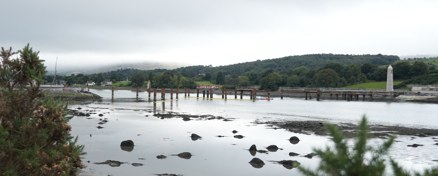 Wide angle view of the river with
concrete abutments on left and right, and a
series of metal posts and frames in the
river.